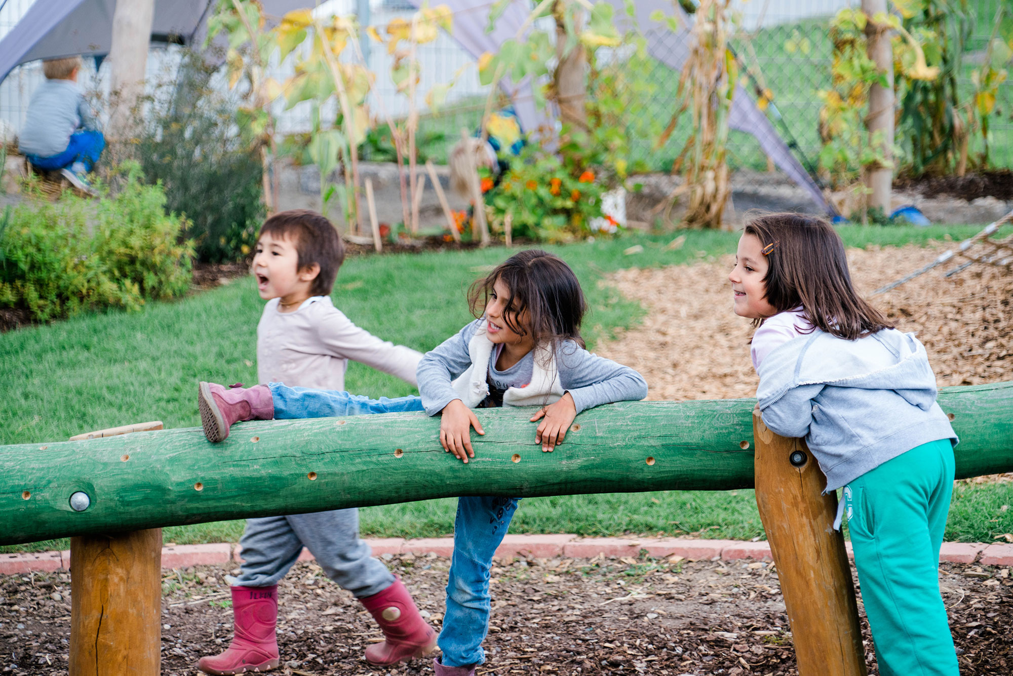 Drei Kinder sind an einem grün angemalten Baumstamm, an dem geklettert oder balanciert werden kann.