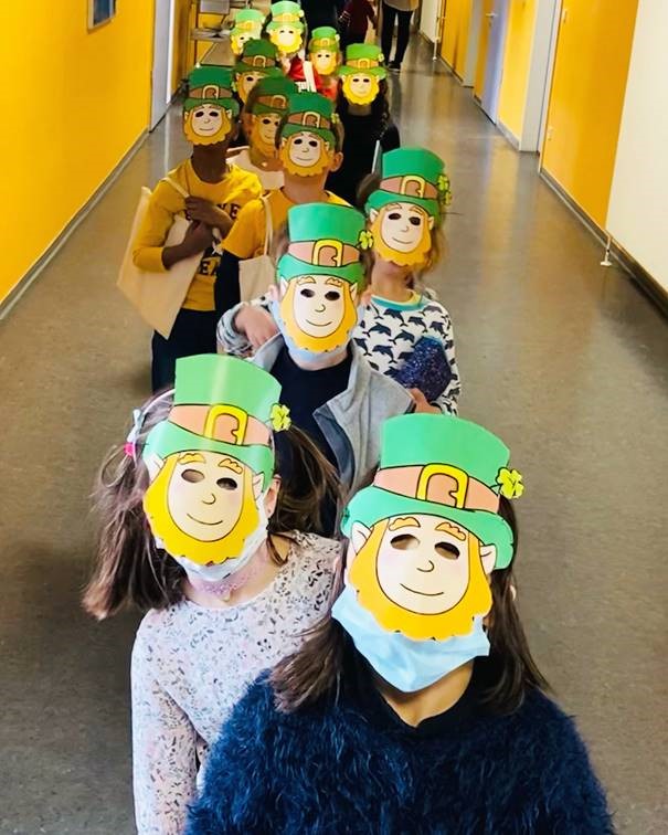 Schülerinnen und Schüler stehen hintereinander in einer Reihe und tragen Leprechaun Masken.