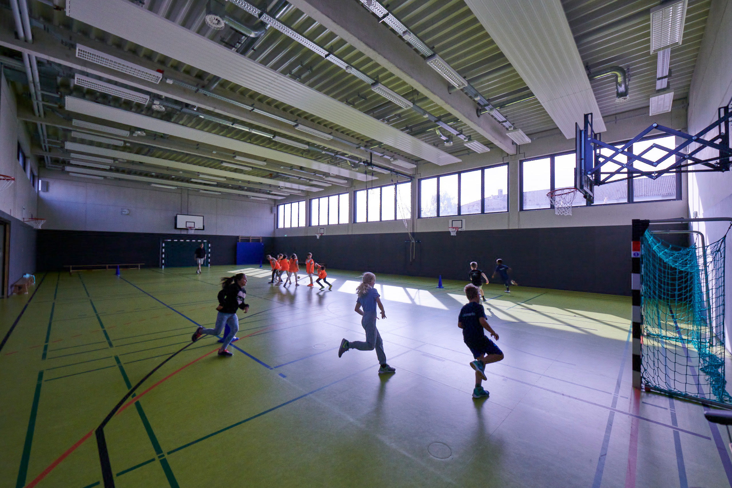 Schülerinnen und Schüler im Sportunterricht in der Turnhalle. Einige rennen durch die Halle.