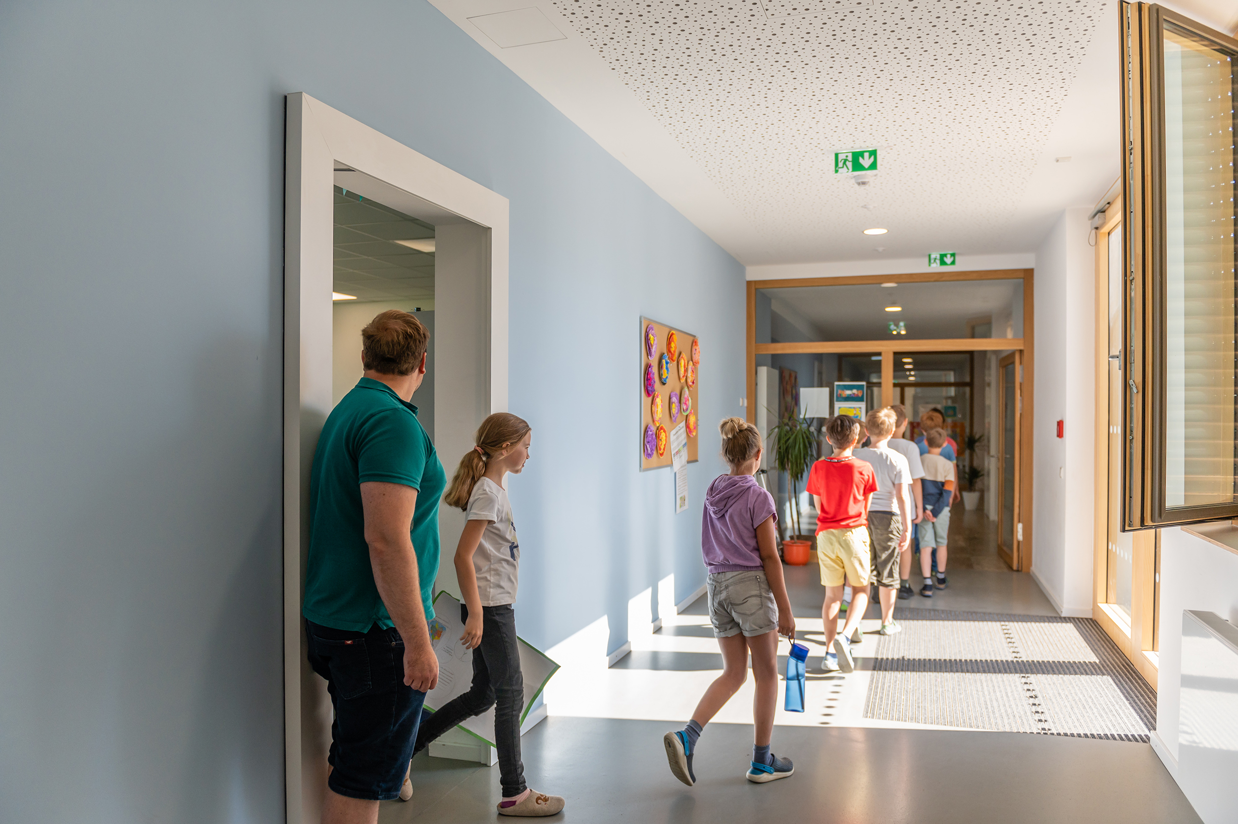 Students come out of the classroom and walk through the corridor. The children can be seen from behind. 