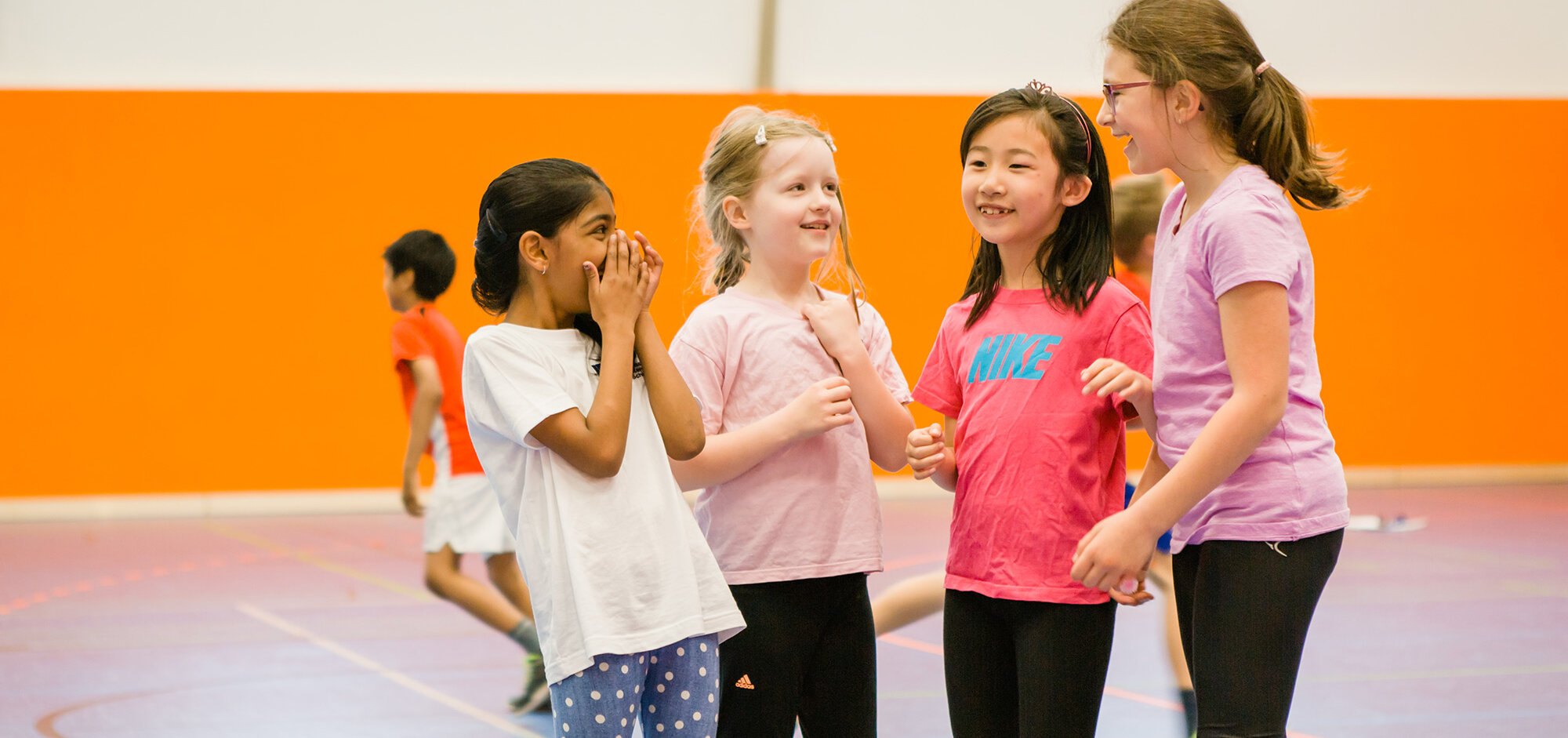 Four girls are standing together in the gym and laughing.