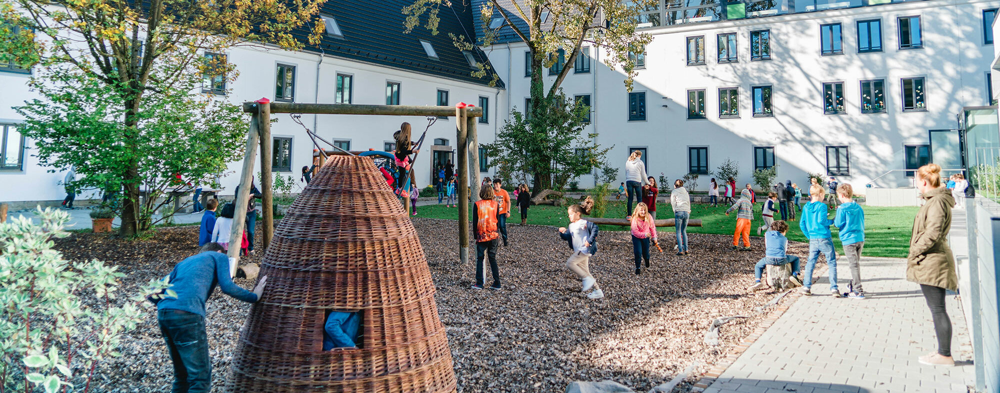 Blick auf den Schul-Innenhof mit zwei Bäumen und spielenden Kindern. 