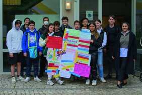 Schülerinnen und Schüler stehen für ein Gruppenfoto vor dem Schulgebäude und halten ein Plakat