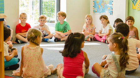 Kindergartenkinder sitzen im Kreis auf dem Boden im Gruppenraum.