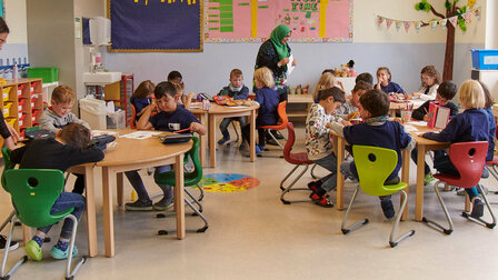 Blick in den Kindergarten-Gruppenraum. Alle Schülerinnen und Schüler sitzen an ihren Plätzen.