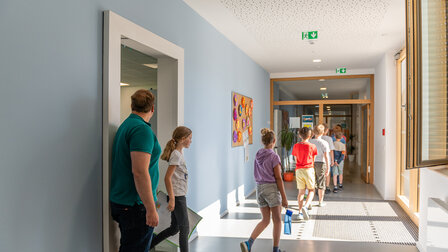 Students come out of the classroom and walk through the corridor. The children can be seen from behind. 