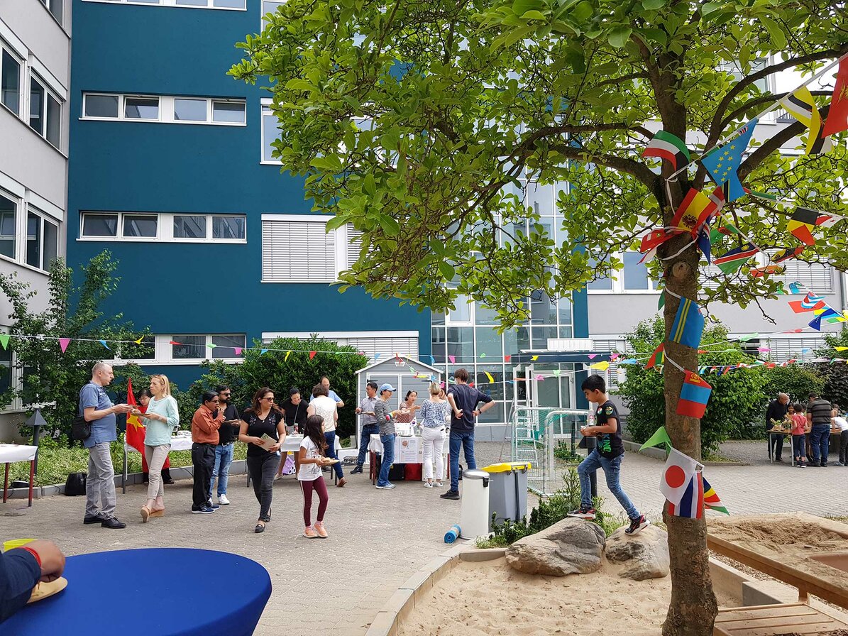View of the schoolyard. Colourful flags and pennant strings are stretched. Parents and students can be seen.