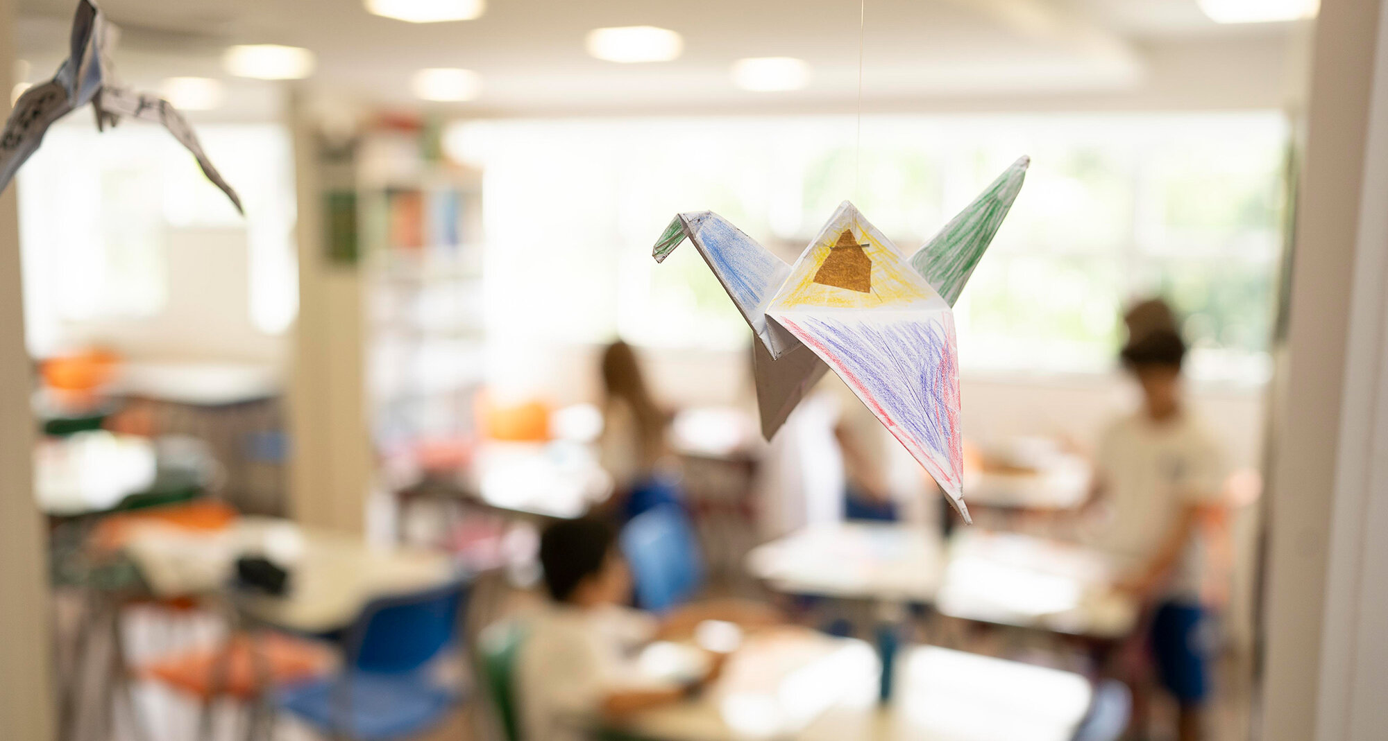 A handmade, painted origami crane hangs in the classroom, which fades into the background.	