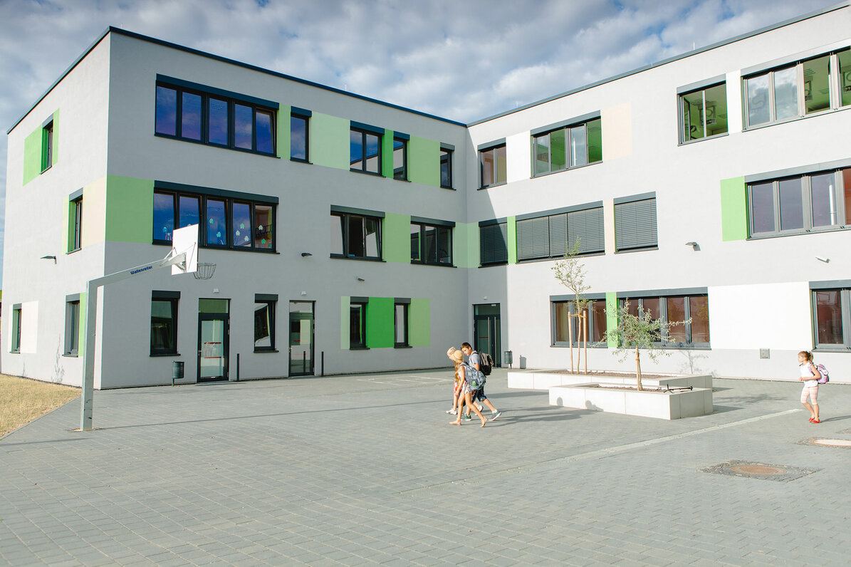 Man sieht das Schulgebäude mit Schulhof, in dem man auch Basketball spielen kann.