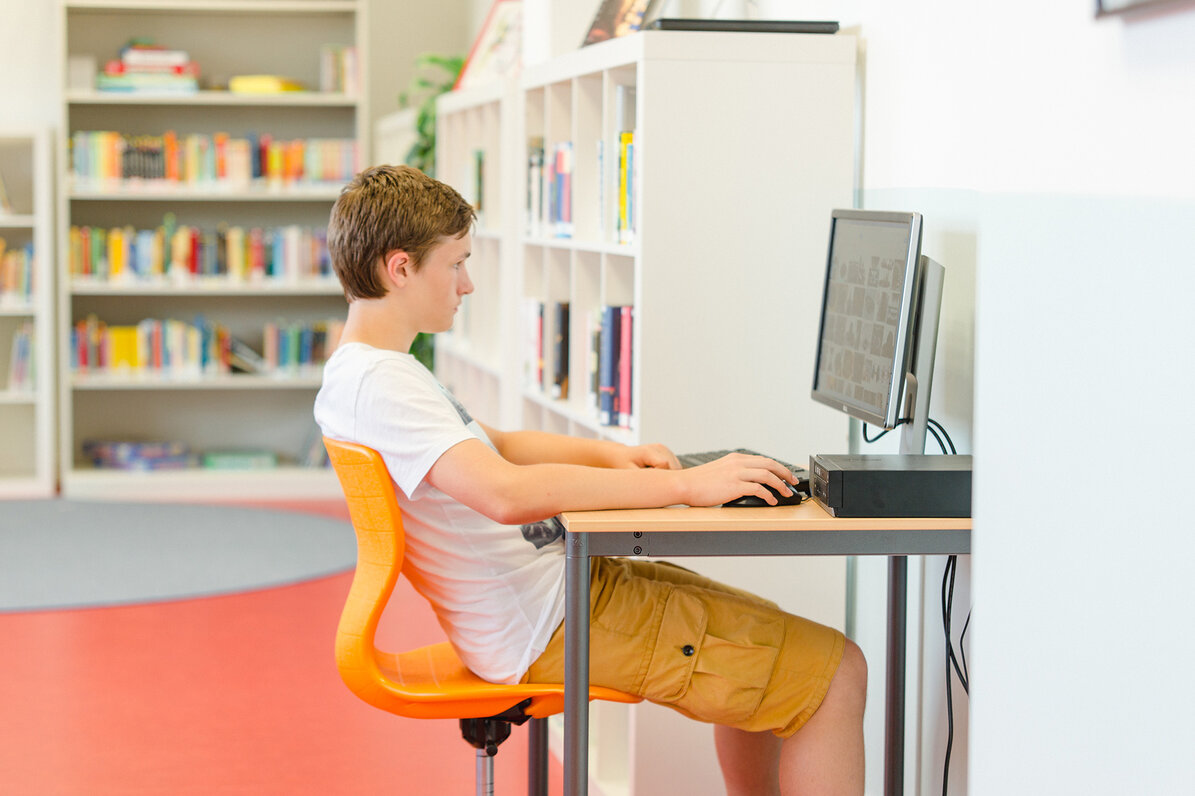 A student is sitting in front of a computer in the media library. 