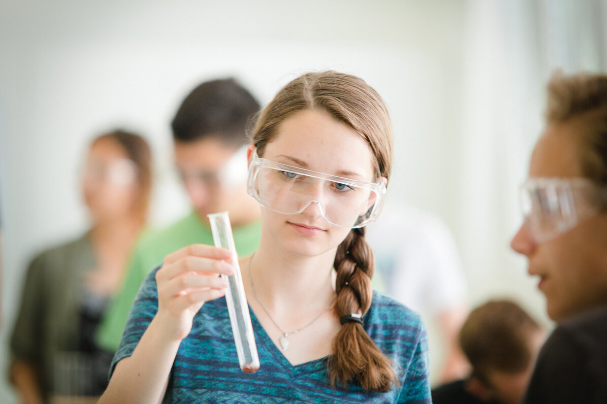 Eine Schülerin hat eine Schutzbrille an und ein Reagenzglas in der Hand. 