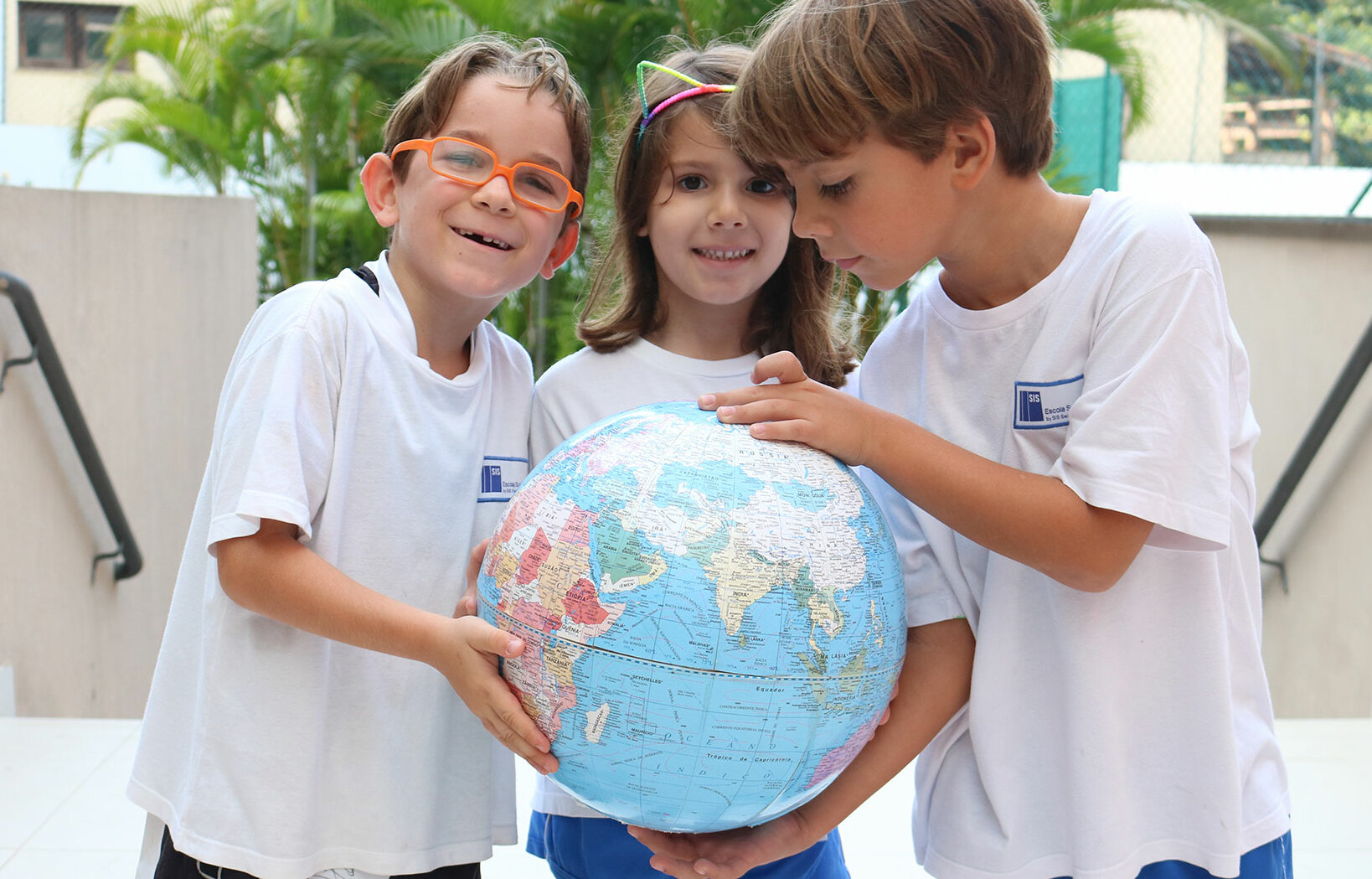 Three children hold a round globe in their hands together.	