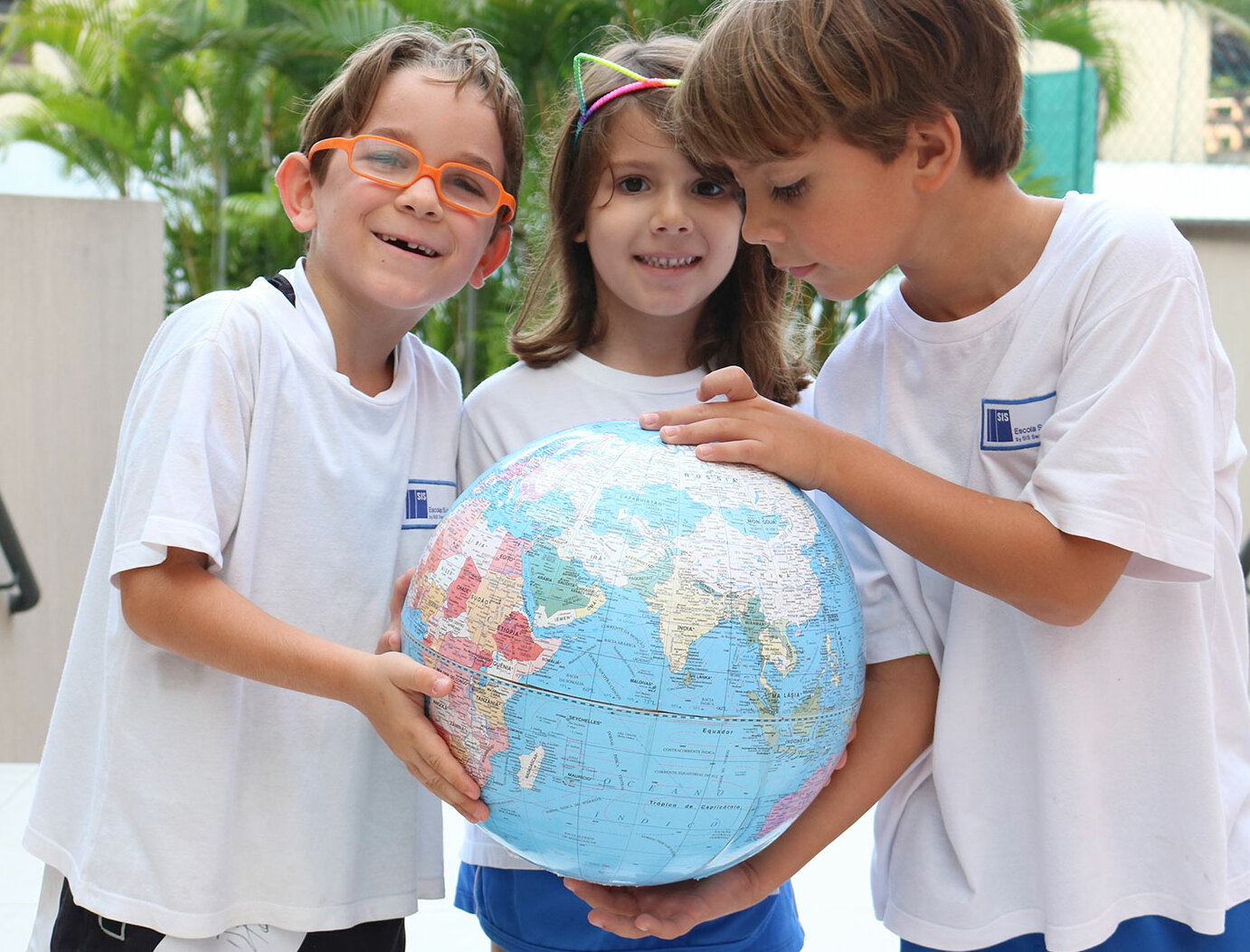 Drei Kinder halten gemeinsam mit ihren Händen einen runden Globus in ihren Händen.	