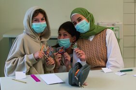 Drei Schülerinnen am Tisch im Klassenzimmer. Sie tragen medizinische Masken.