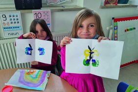 Zwei Mädchen halten ihre gemalten Schmetterlinge hoch