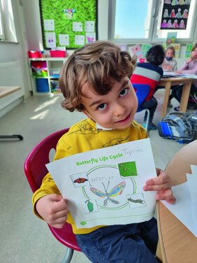 Ein Junge zeigt sein Arbeitsblatt mit gemaltem Schmetterling und Lebenszyklus