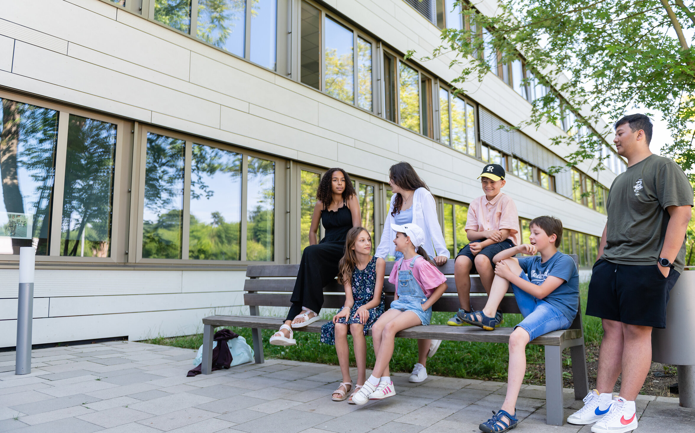 Students of different ages sit on a bench in front of the school building.
